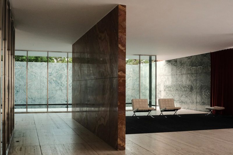A modern room with a large, open space featuring a wall of windows, a row of chairs, and a black rug.