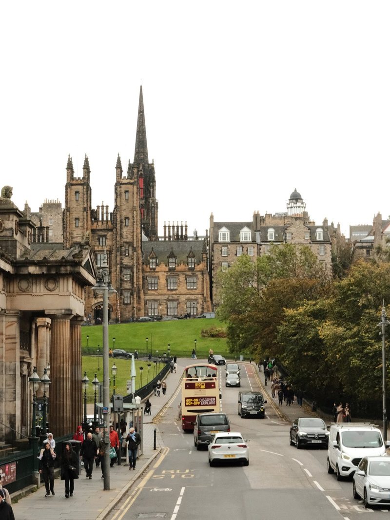 A city street with a prominent church steeple in the background, featuring a double-decker bus and several cars on the road.
