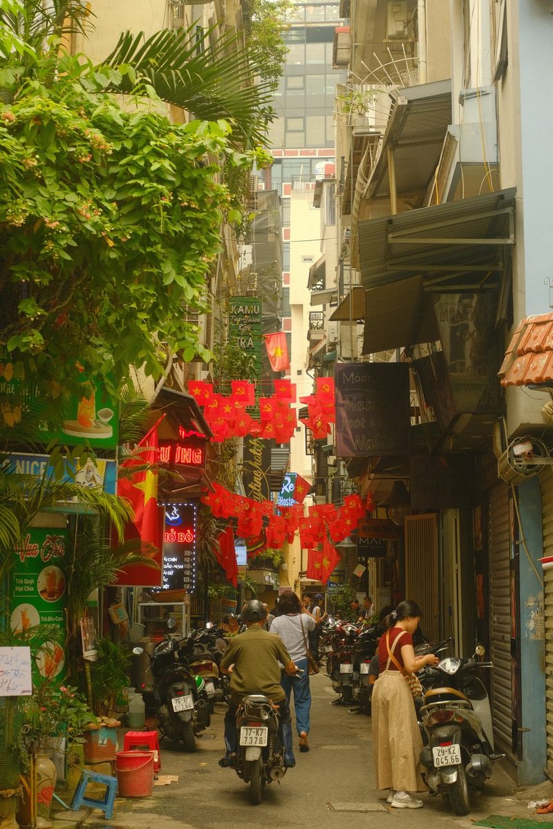 A narrow street in a city with tall buildings, lined with shops and restaurants, and decorated with red lanterns.