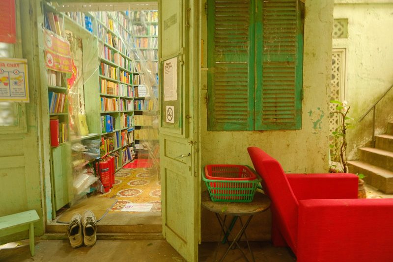 A small, rustic bookstore with a green exterior and a cozy interior, featuring a bookshelf and a red couch.