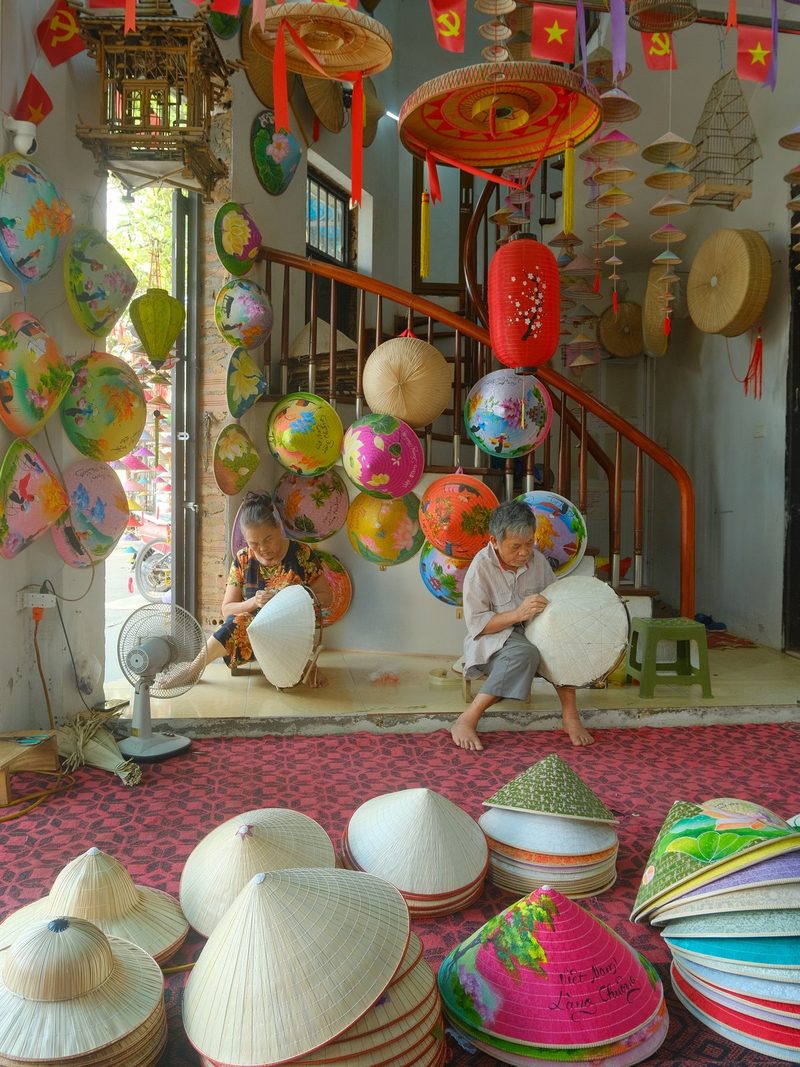 Two children are sitting on the floor in a room filled with colorful hats and lanterns.