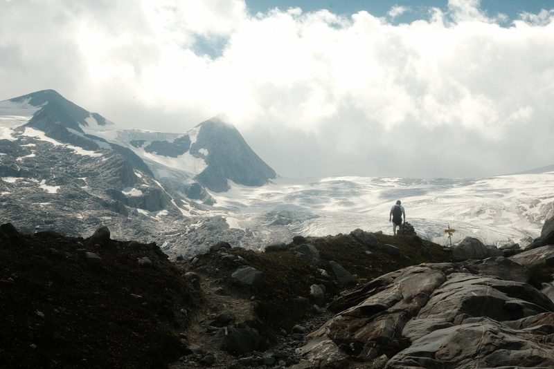 A person hiking on a rocky mountain trail with a glacier in the background.