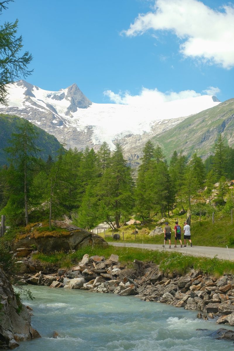 A group of people hiking along a river in a mountainous region.