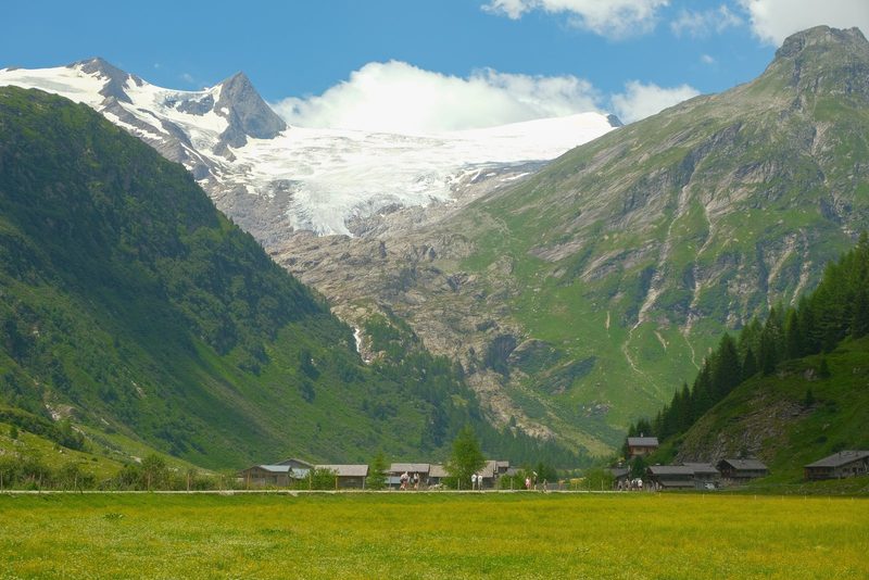 A picturesque valley with a small village and snow-capped mountains in the background.