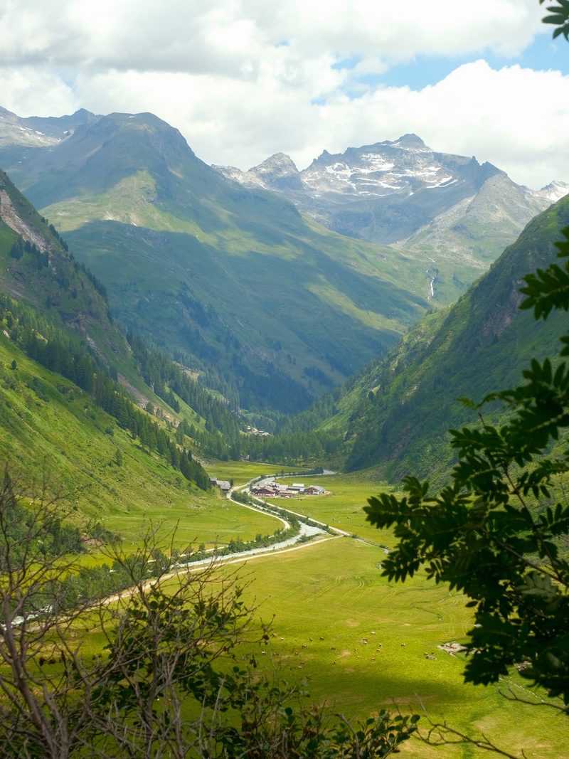 A valley with a river and buildings surrounded by mountains and greenery.