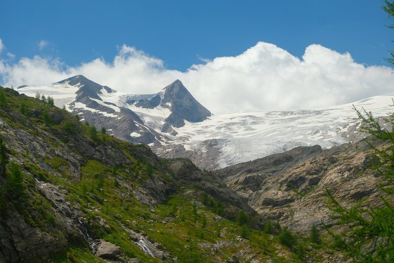 Snow-capped mountain peaks and glaciers under a blue sky with white clouds.