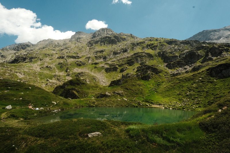 A serene mountain landscape with a small lake and a few people in the distance.