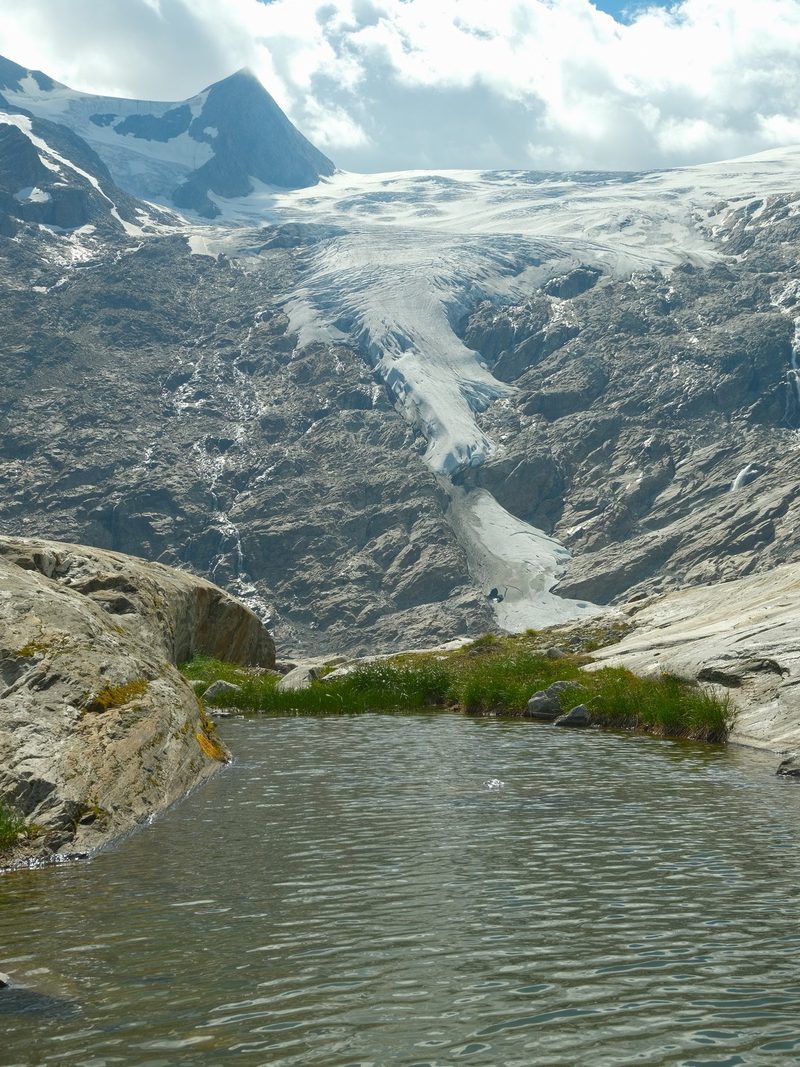 A serene mountainous landscape with a glacier and a small lake.