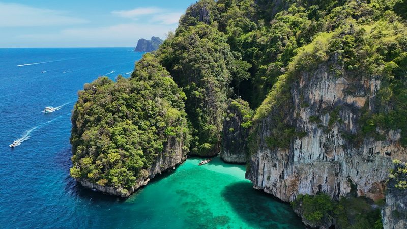 A large, rocky island with lush greenery and a small, turquoise-colored body of water, surrounded by several boats.