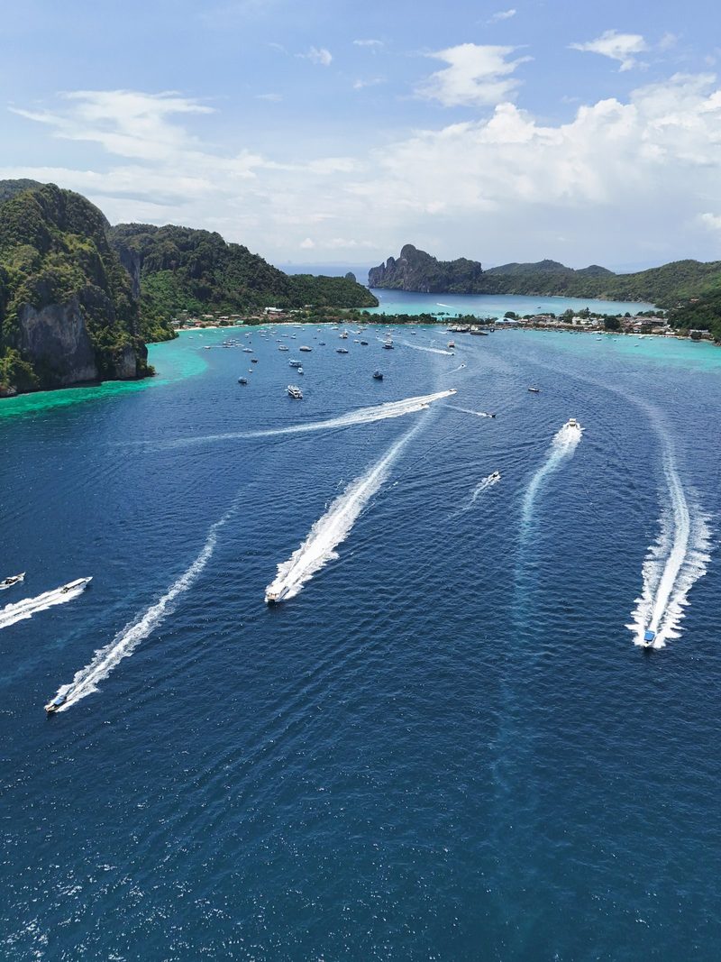A large body of water is filled with numerous boats, some of which are leaving behind white trails in the water.