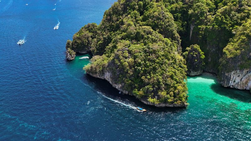 A large island with steep cliffs and dense vegetation is surrounded by deep blue water, with a boat speeding by on the left side.