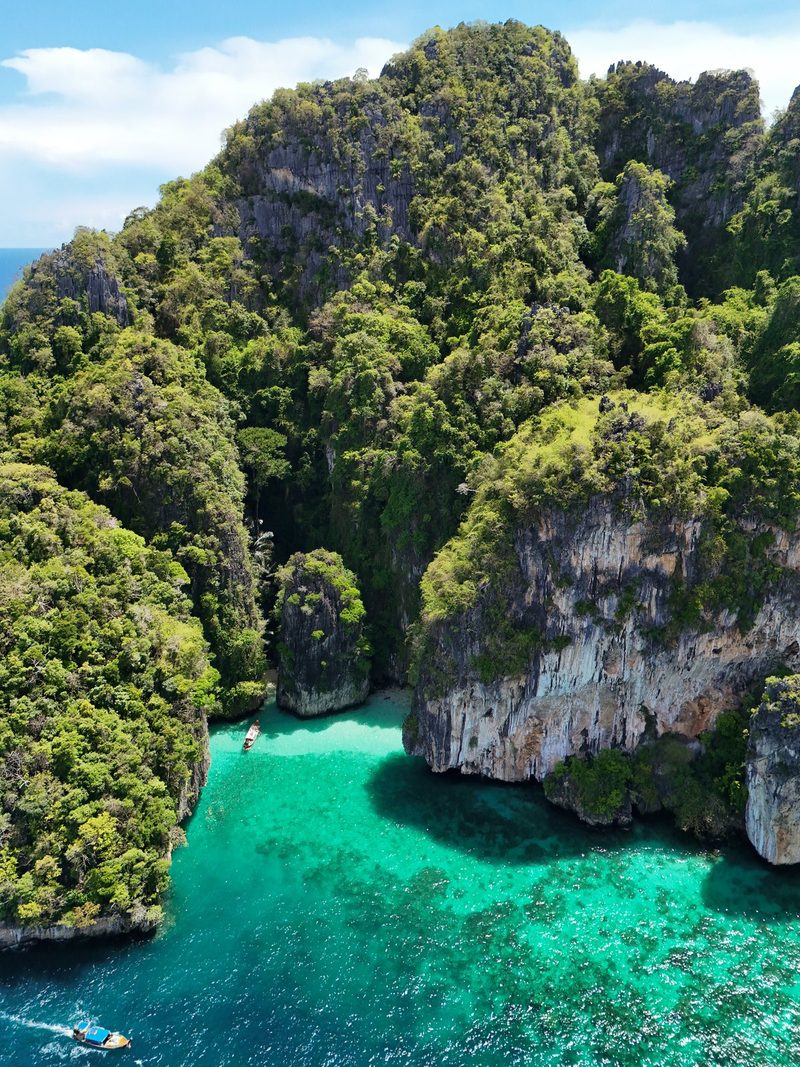 A large rocky cliff rises from a turquoise sea, with two boats in the water below.