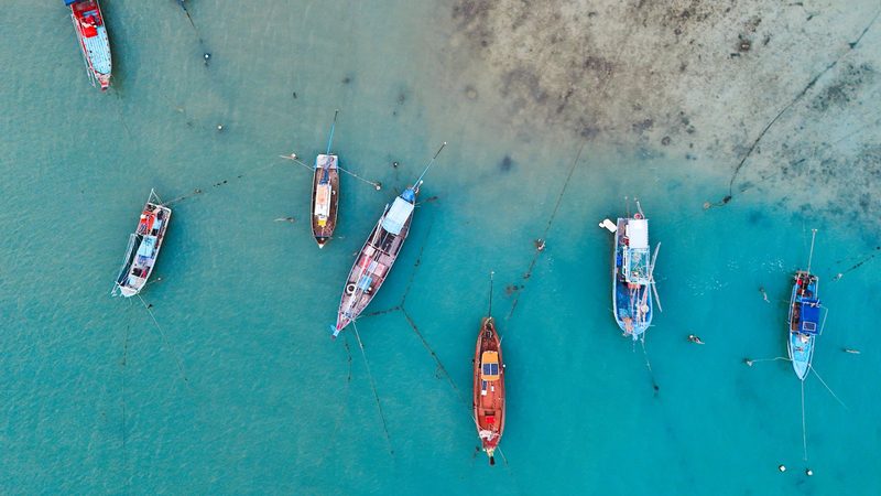 Aerial view of a group of boats floating in a body of water, with some boats partially submerged in the shallow water.