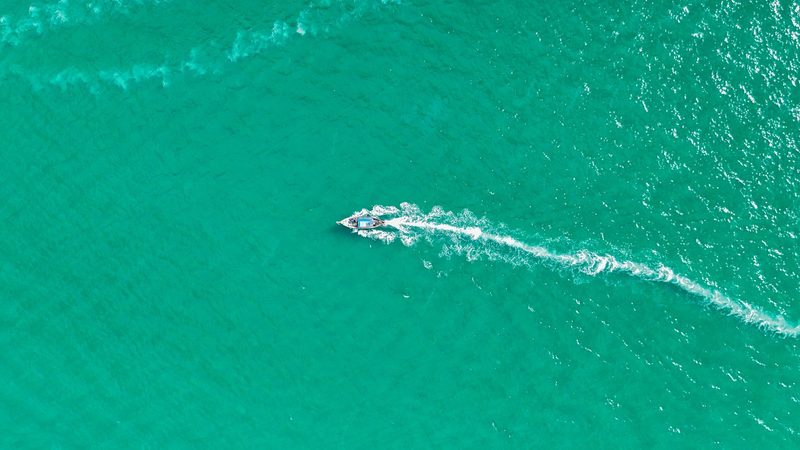 A boat with a white wake trails behind it, leaving a path of disturbed water in its wake.