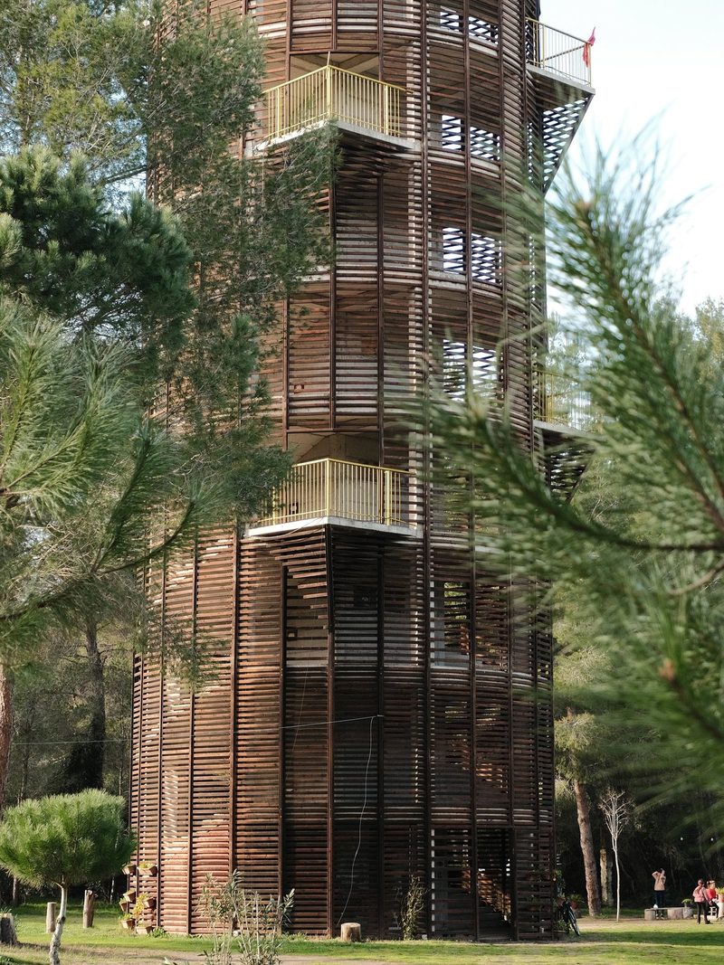 A tall, multi-level wooden structure with a metal railing, surrounded by trees and greenery.