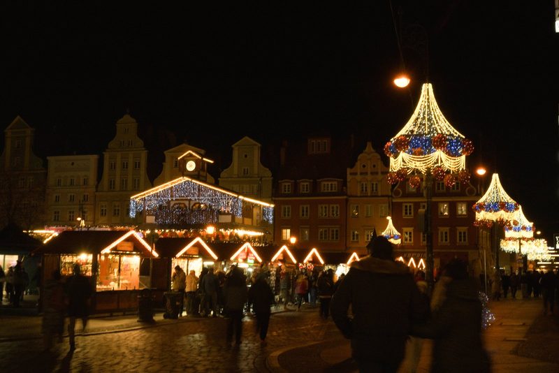 The image depicts a festive scene at night, featuring a large building adorned with numerous lights and decorations, including a prominent Christmas tree.