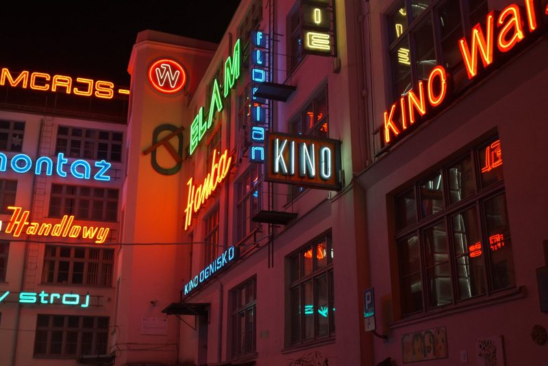 A building with multiple neon signs, including "KINO" and "W", is illuminated at night.