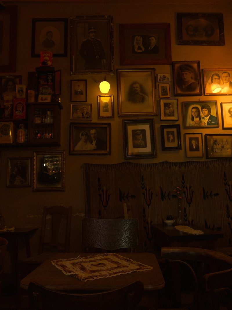 A dimly lit room with a collection of framed photographs on the walls, featuring a mix of portraits and group shots, with some images in sepia tone and others in color.