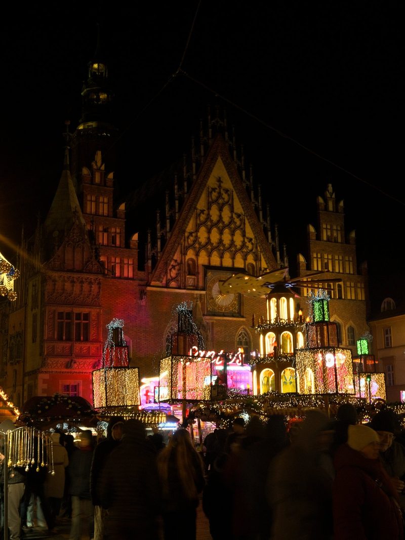 A large building with a clock tower and a crowd of people in front of it, decorated with colorful lights and Christmas decorations.