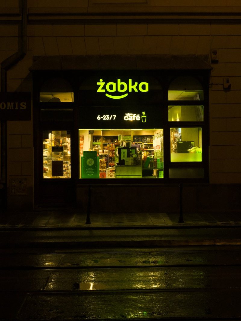 A storefront with a sign reading "zabka" and a window displaying various products, including a green sign with white text.