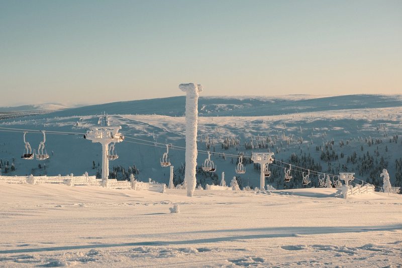 A snowy landscape with a ski lift and trees in the background, featuring a clear blue sky.