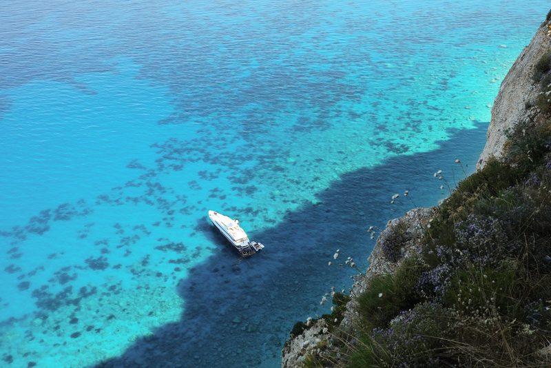A boat floats in a body of water, surrounded by a rocky cliff and lush greenery.