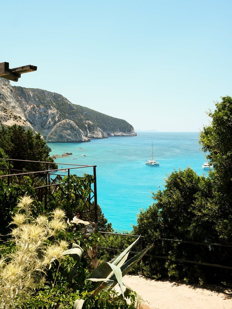 A serene scene featuring a body of water, surrounded by lush greenery and a few boats, with a mountainous landscape in the background.