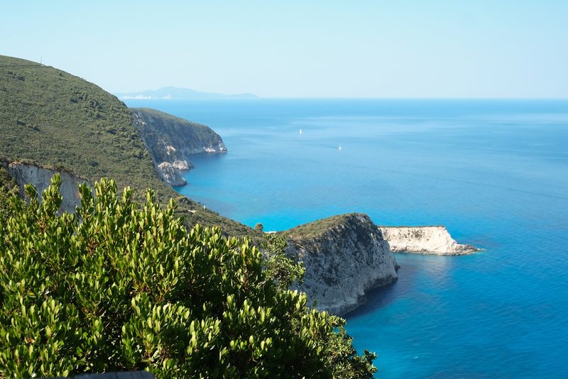 A cliff-lined coastline with a prominent white rock formation, surrounded by lush greenery and a deep blue sea.