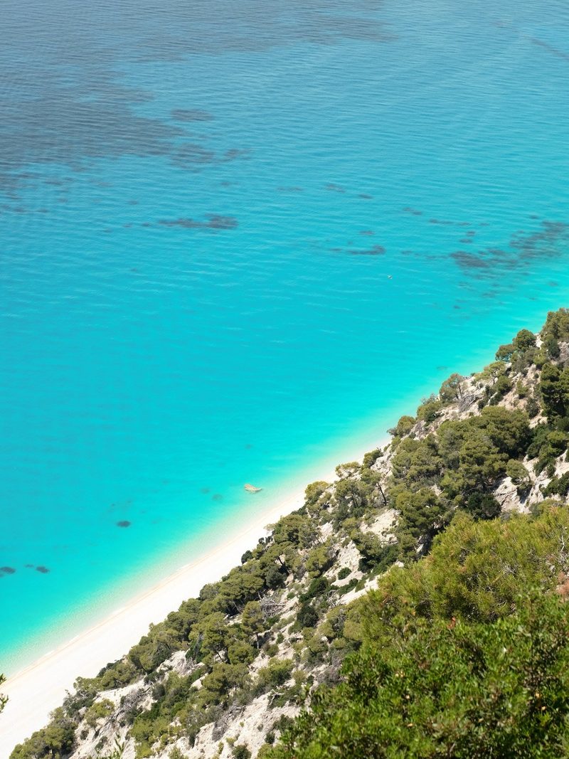 A serene beach scene features a white sand shoreline, a vibrant turquoise sea, and a lush green hillside.