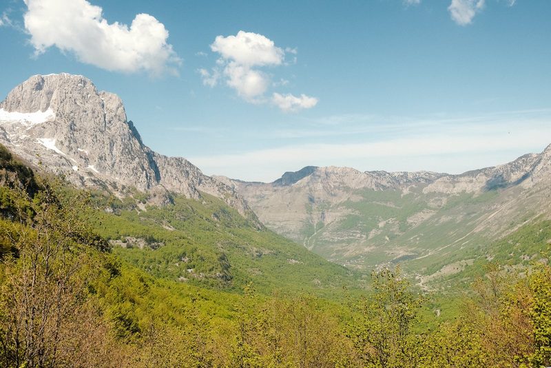 A mountain range with a valley and greenery in the foreground.