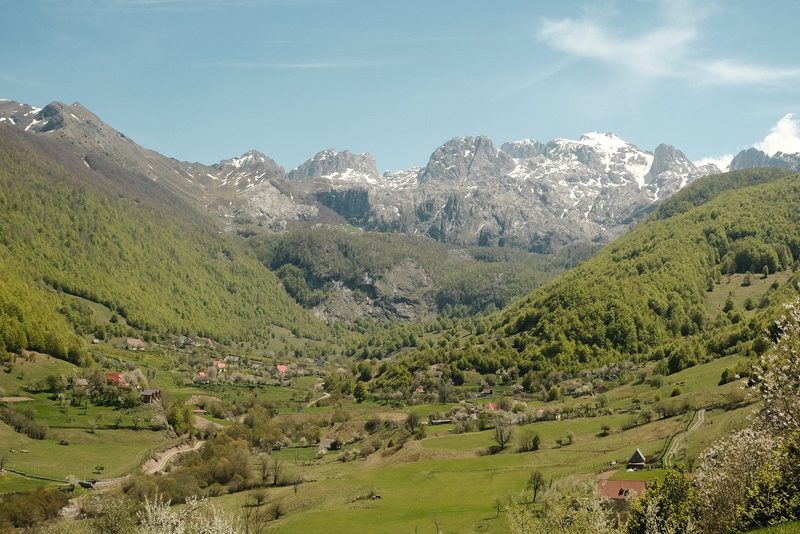 A mountainous valley with a small village and snow-capped peaks in the background.