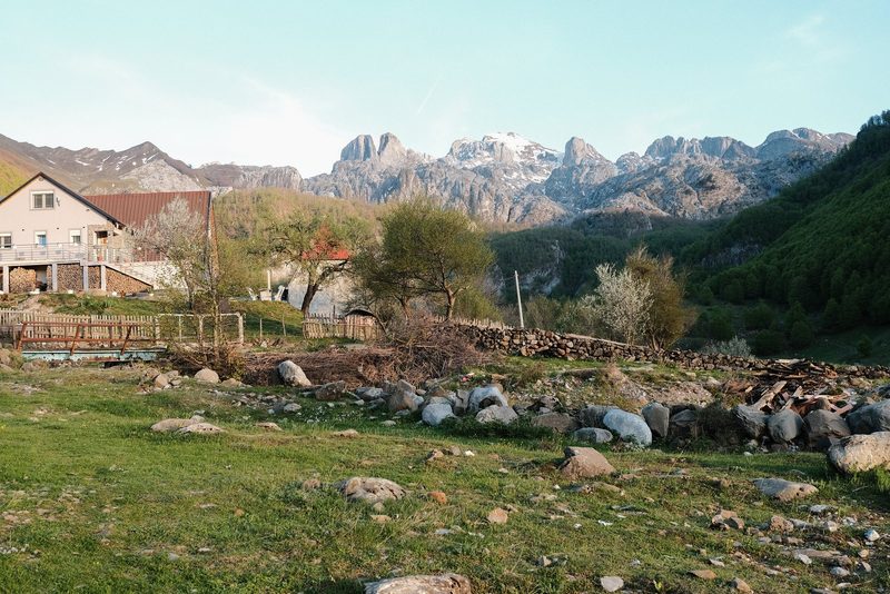 A serene mountainous landscape with a house and a field of rocks and grass.