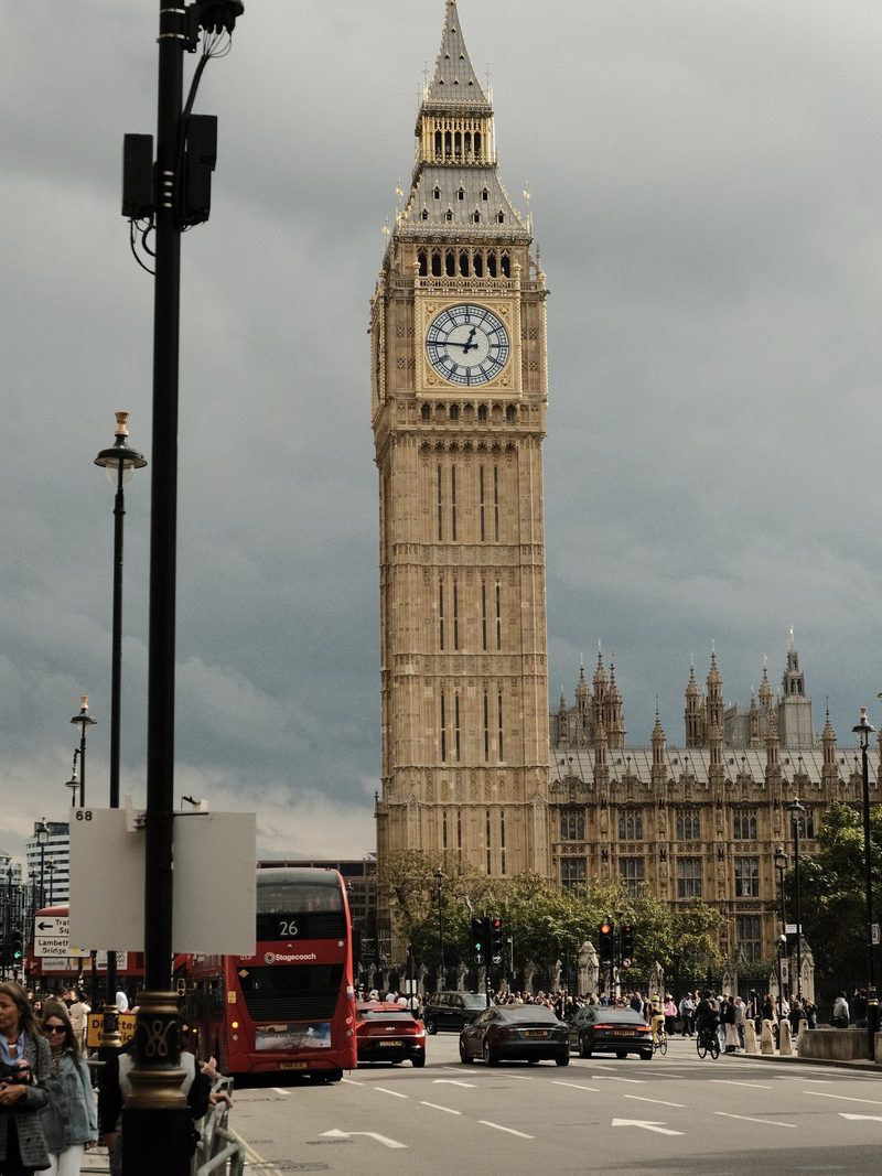 A large clock tower in the center of a city, surrounded by cars and buses.