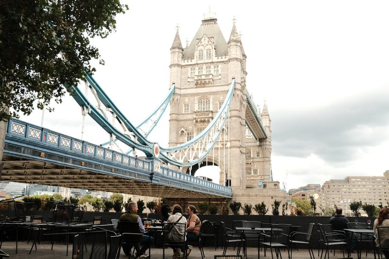 A group of people sitting at tables in front of the Tower Bridge in London.