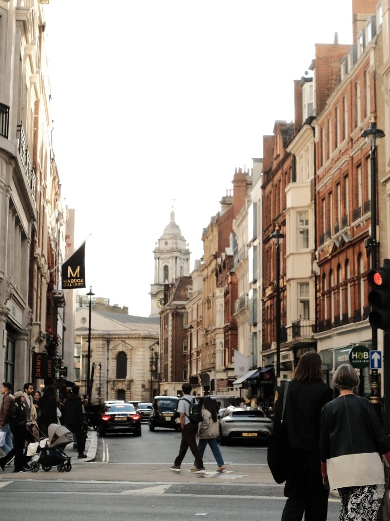 A city street with tall buildings and a church steeple in the distance.