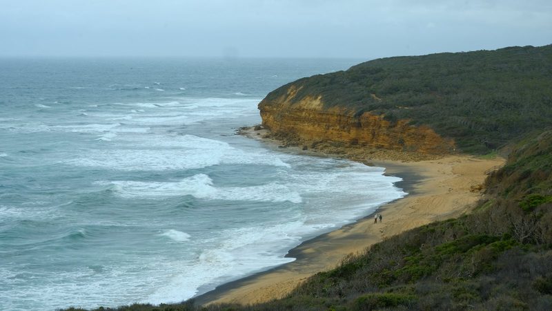 A cliff-lined beach with a sandy shore and a rugged coastline under a cloudy sky.