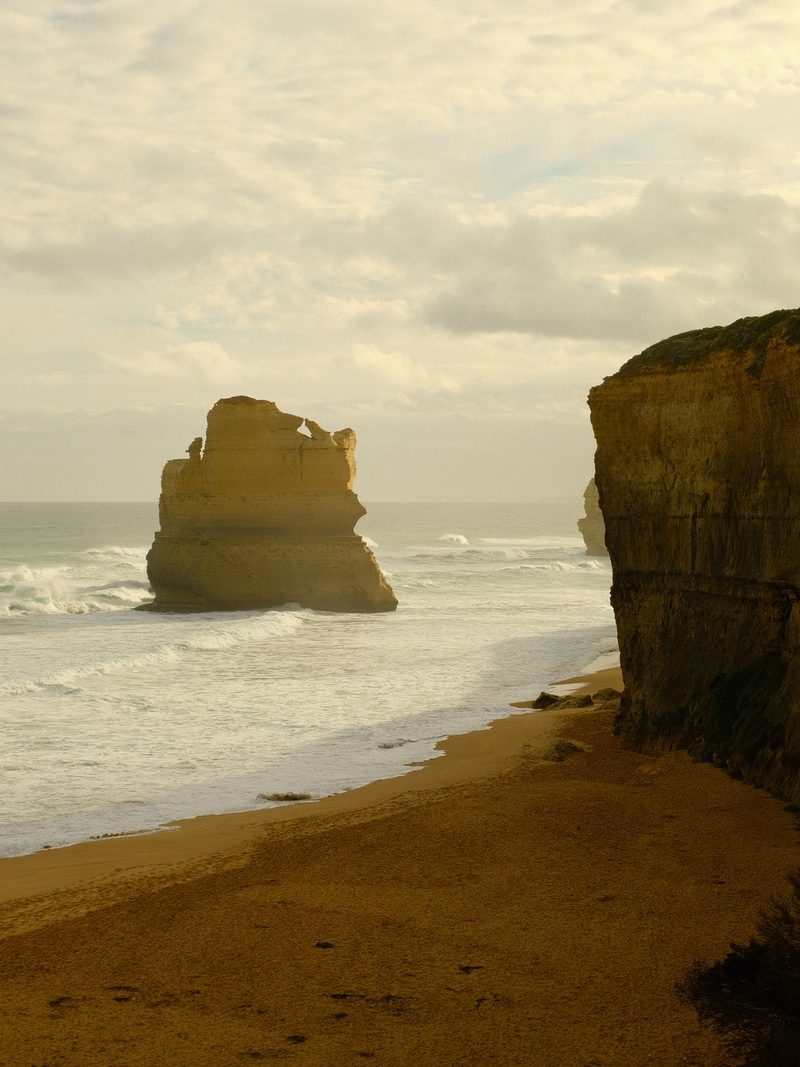 A large rock formation stands in the ocean, with a cliff face on the right side.