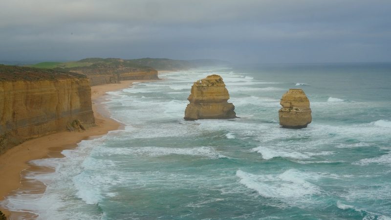 A coastal landscape with cliffs, sandy beach, and large rock formations in the ocean.