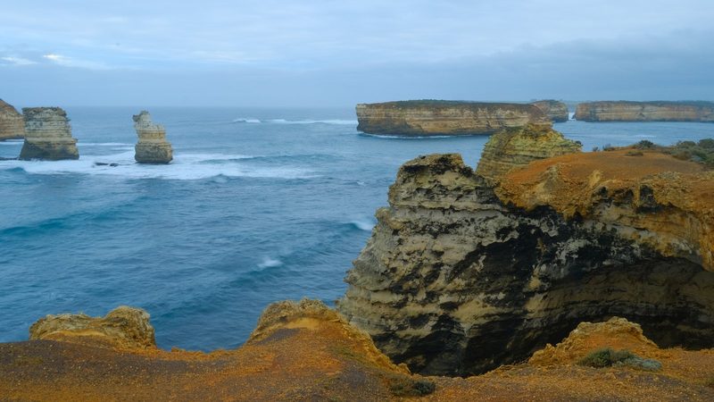 A rugged coastline with large rock formations and a vast ocean under a cloudy sky.