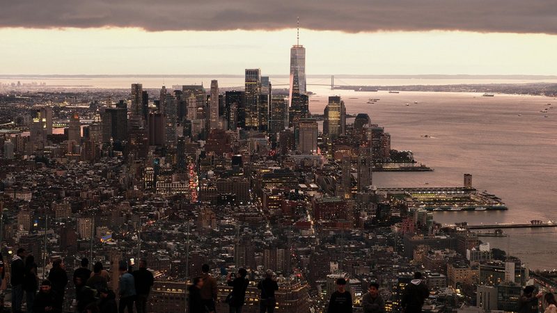 A cityscape with a large body of water and a bridge in the distance, featuring a densely populated urban area with numerous tall buildings and skyscrapers.
