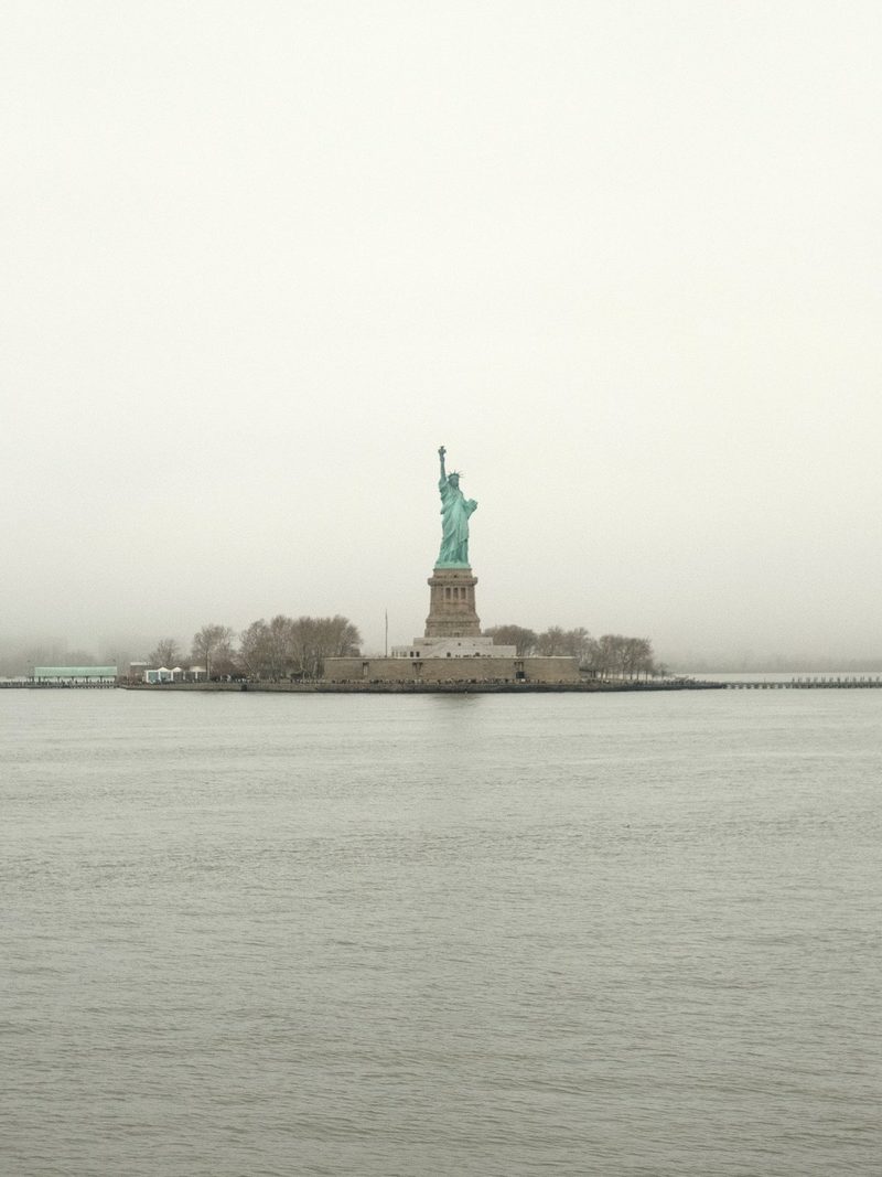 The Statue of Liberty stands on a small island in the water, surrounded by a foggy atmosphere.