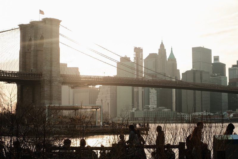 A cityscape with a bridge, skyscrapers, and a river, featuring people in the foreground.