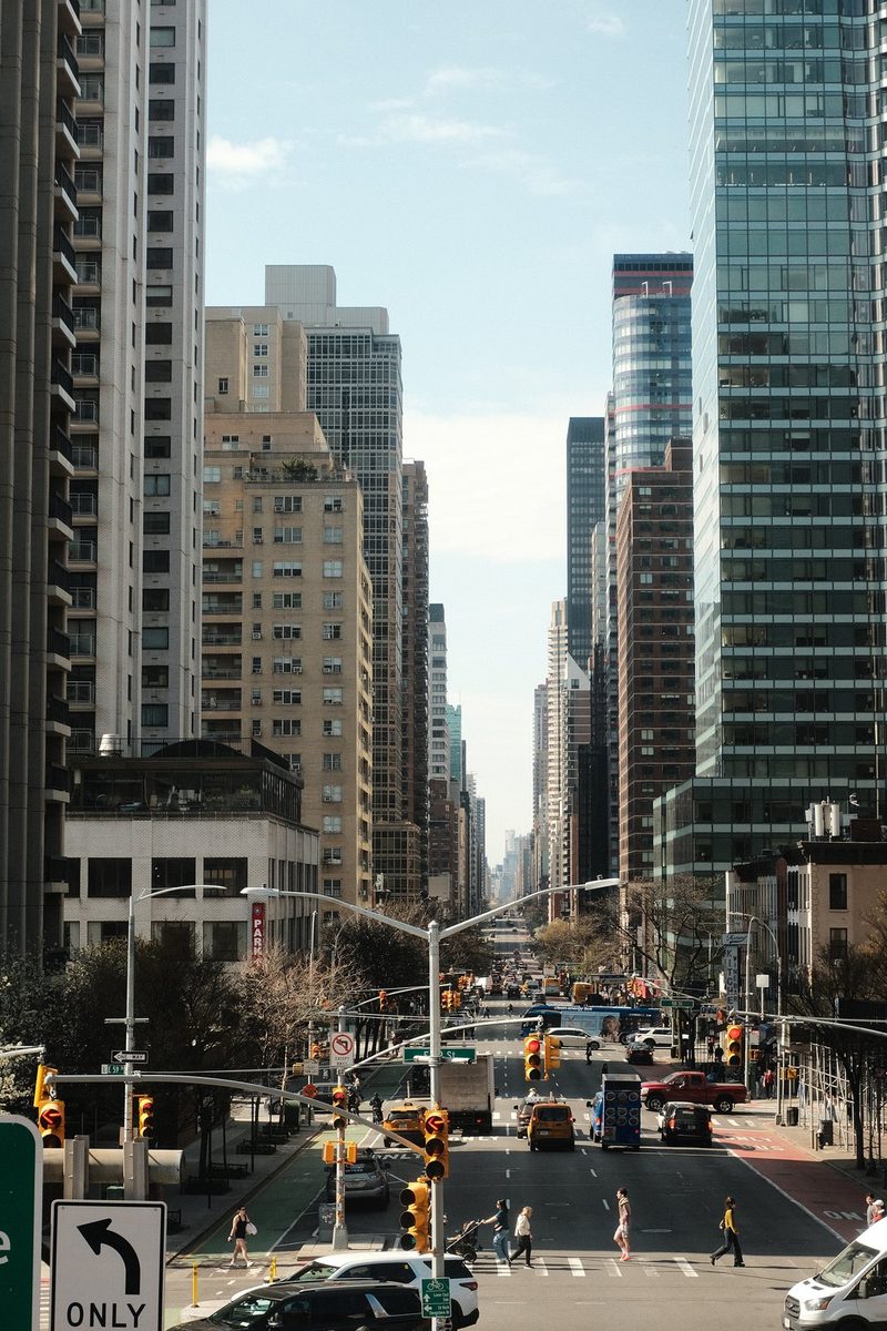 A city street with tall buildings and traffic lights, featuring a busy road with cars and pedestrians.