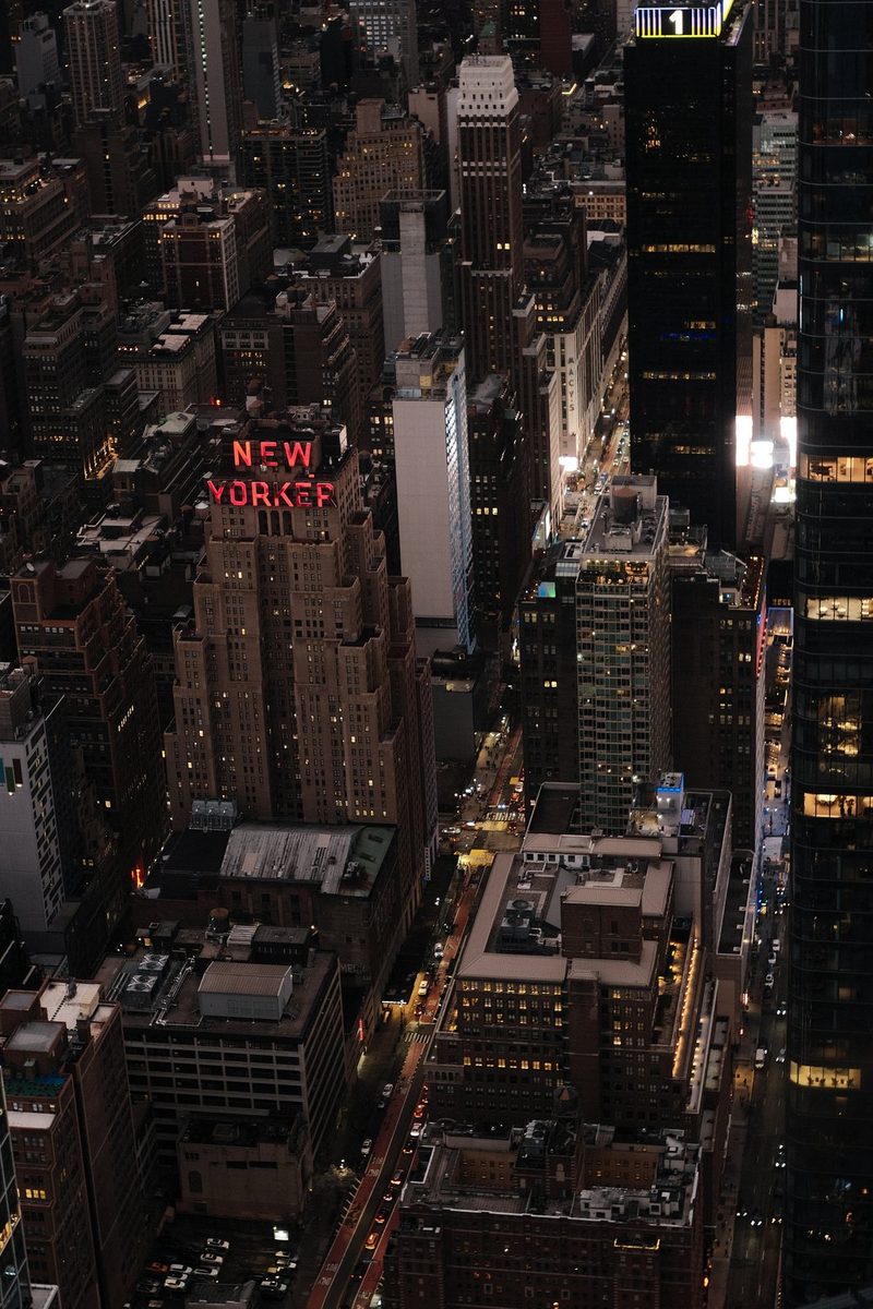 A nighttime aerial view of a densely populated urban area, with a prominent sign reading 'New Yorker' in red letters.