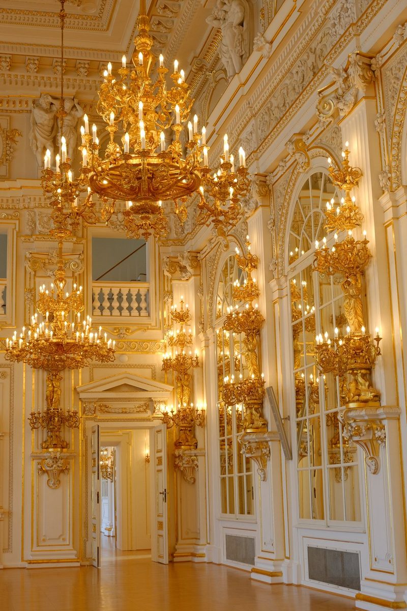 A grand room with ornate gold and white decorations, featuring large chandeliers and mirrors.