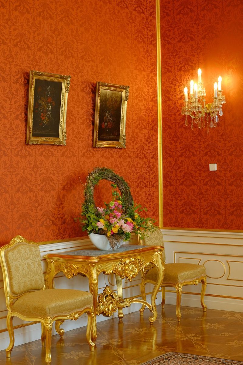 A luxurious room with red wallpaper, gold accents, and a floral arrangement on a table.
