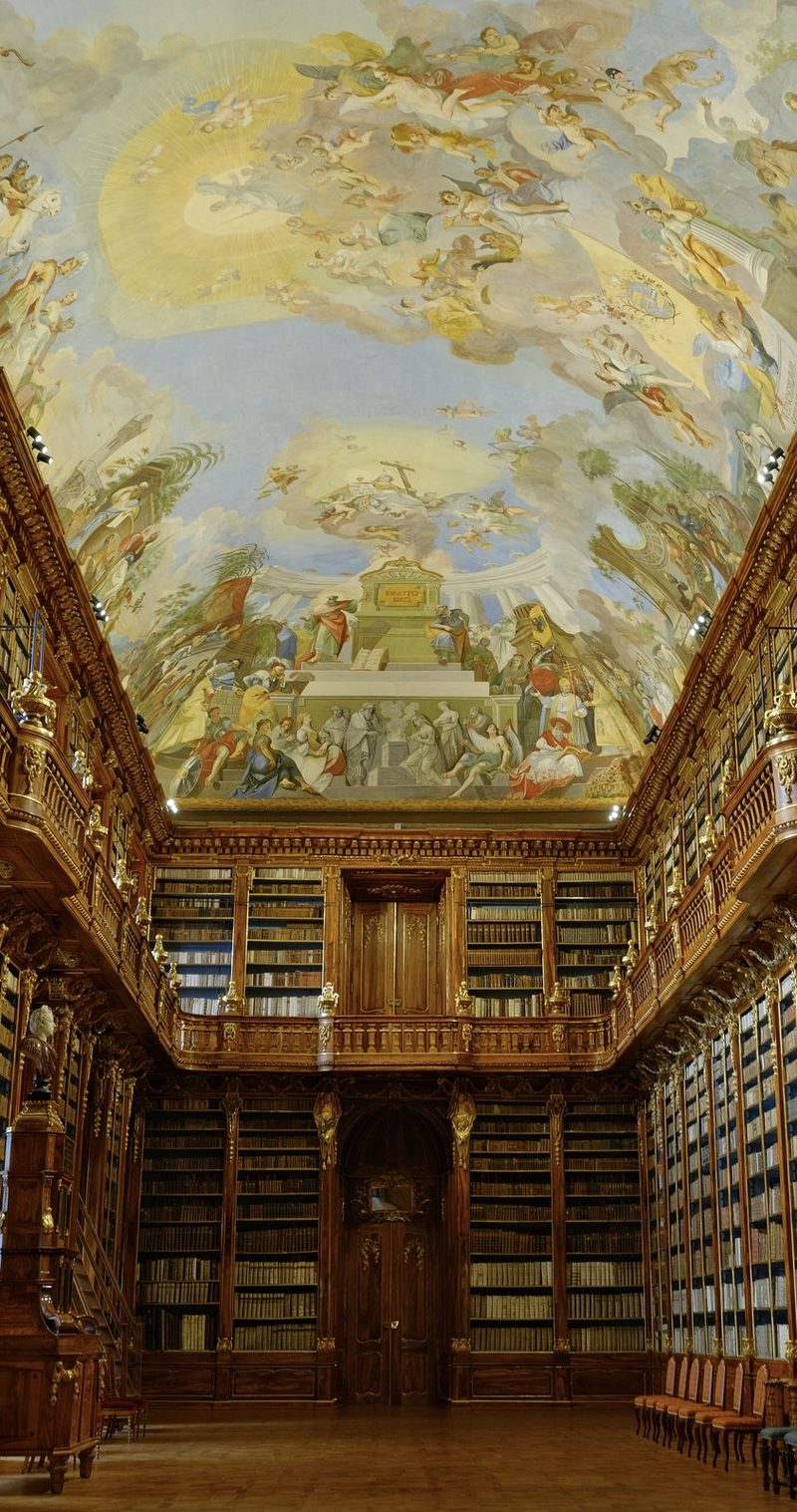A large library with ornate woodwork and a mural on the ceiling.