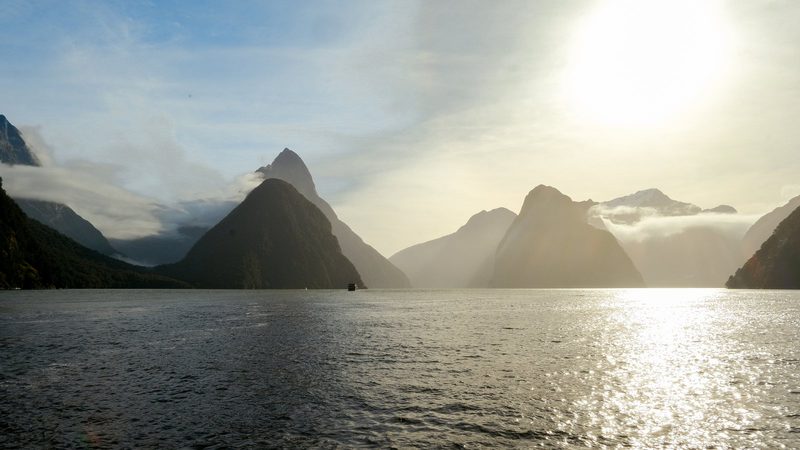 A serene mountainous landscape with a large body of water in the foreground.