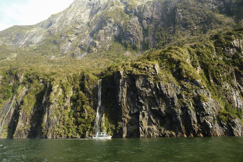 A boat is in front of a large cliff with a waterfall.