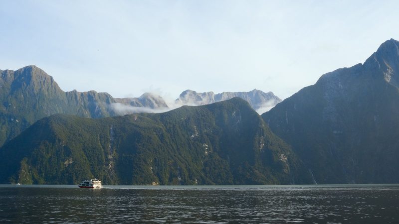 A large boat navigates a vast body of water in front of a mountain range.